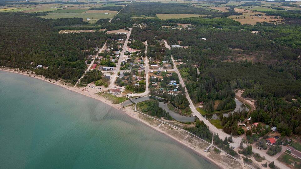 An aerial view of a coastal town with a beach, roads, and surrounding forest.