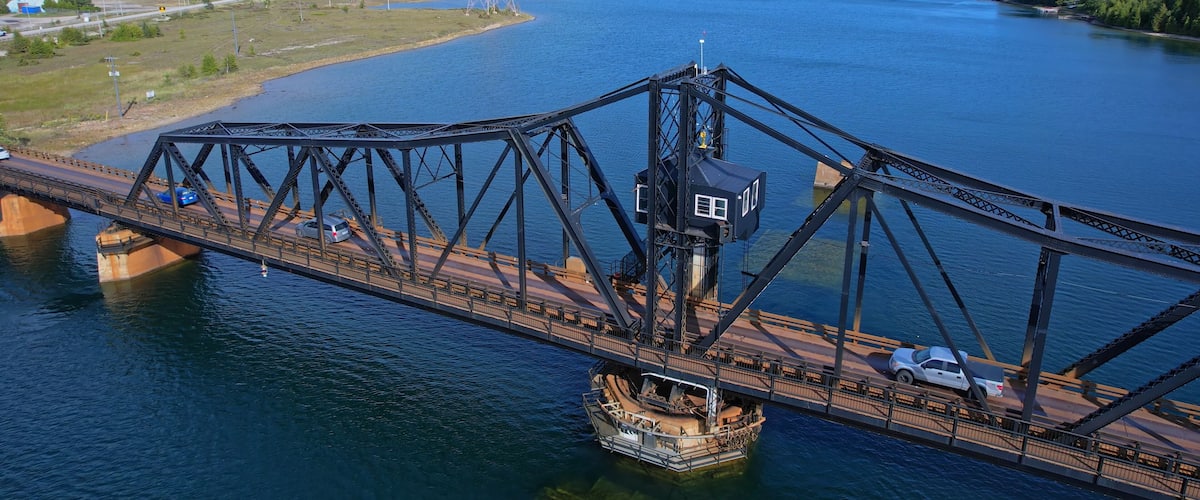 A large steel bridge spanning a wide river, with a boat docked beneath it.