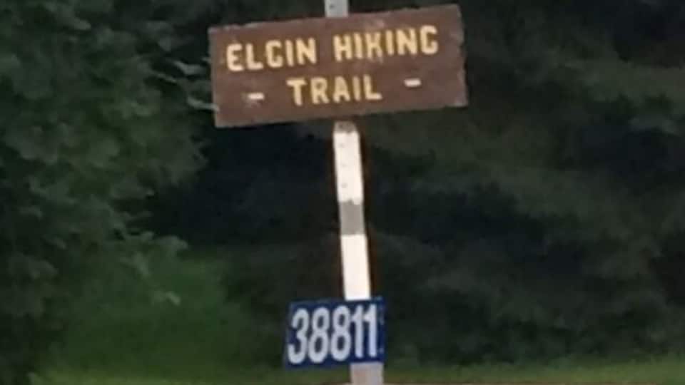 A sign for Elgin Hiking Trail with a stone base and a blue number plate.