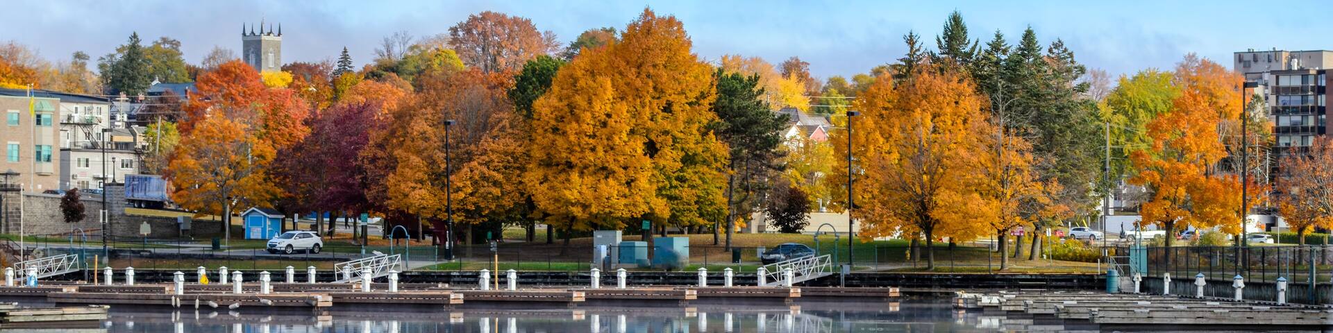 A calm lake reflecting autumn trees and a distant church tower.