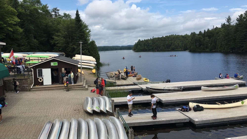 A lakeside dock with canoes, a small cabin, and people around.