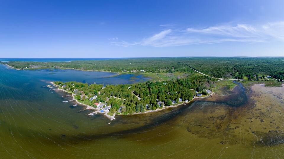An aerial view of a coastal area with a large body of water, a forested peninsula, and a small settlement.