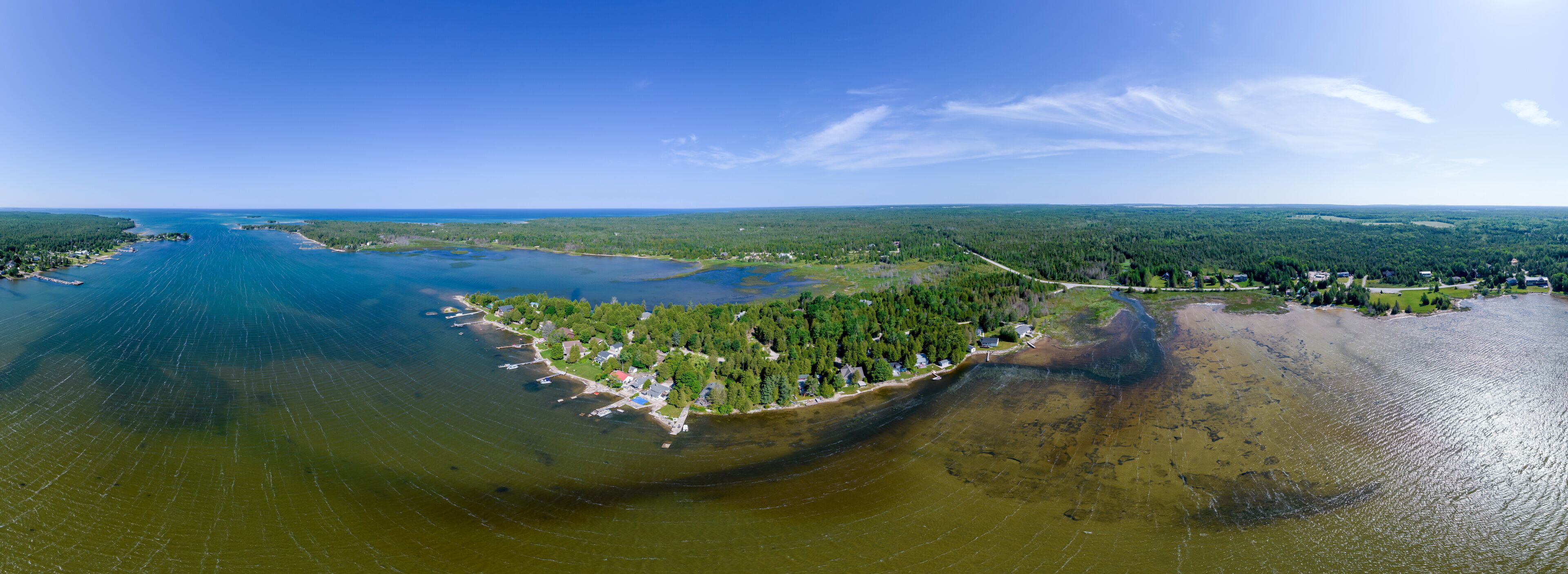 An aerial view of a coastal area with a large body of water, a forested peninsula, and a small settlement.