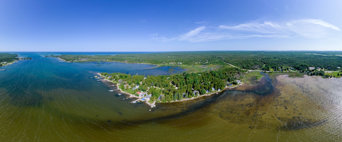 An aerial view of a coastal area with a large body of water, a forested peninsula, and a small settlement.