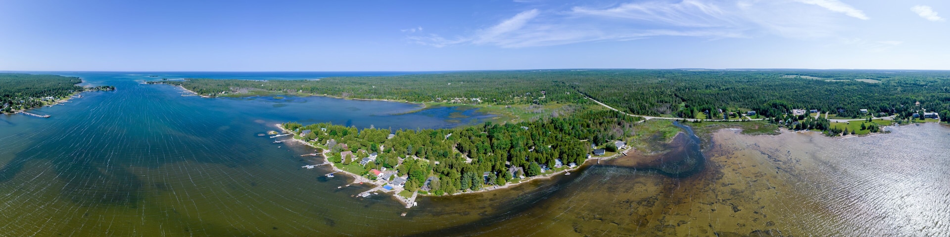 An aerial view of a coastal area with a large body of water, a forested peninsula, and a small settlement.