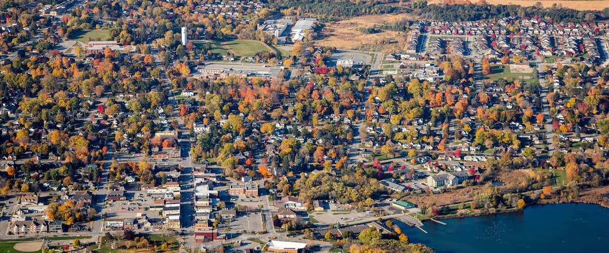 An aerial view of a town with a river, surrounded by autumn-colored trees and various buildings.