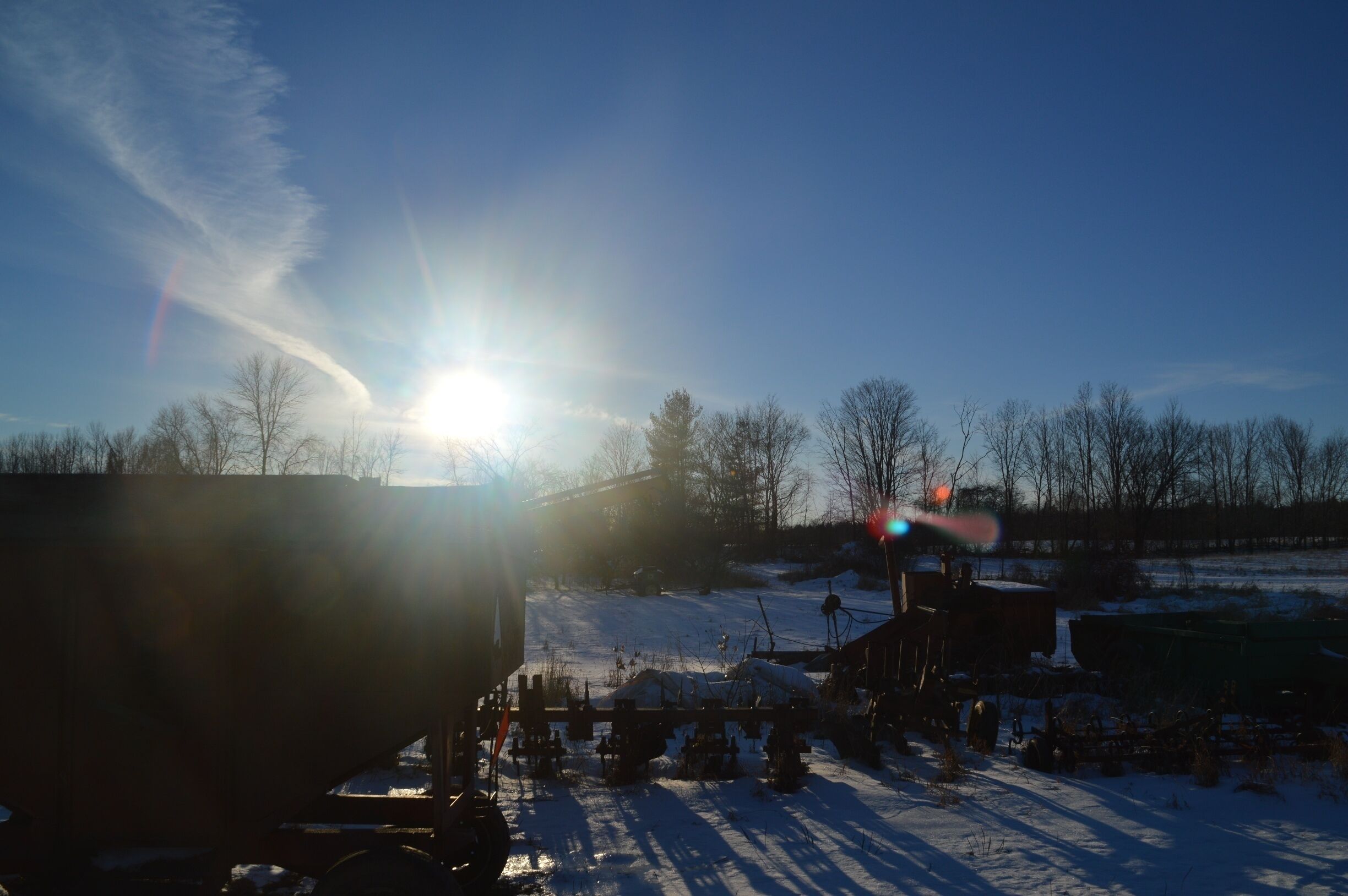 A snowy landscape with a clear sky, a fence, and some trees.