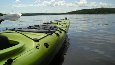 A green kayak on calm water with a forested shoreline in the background.