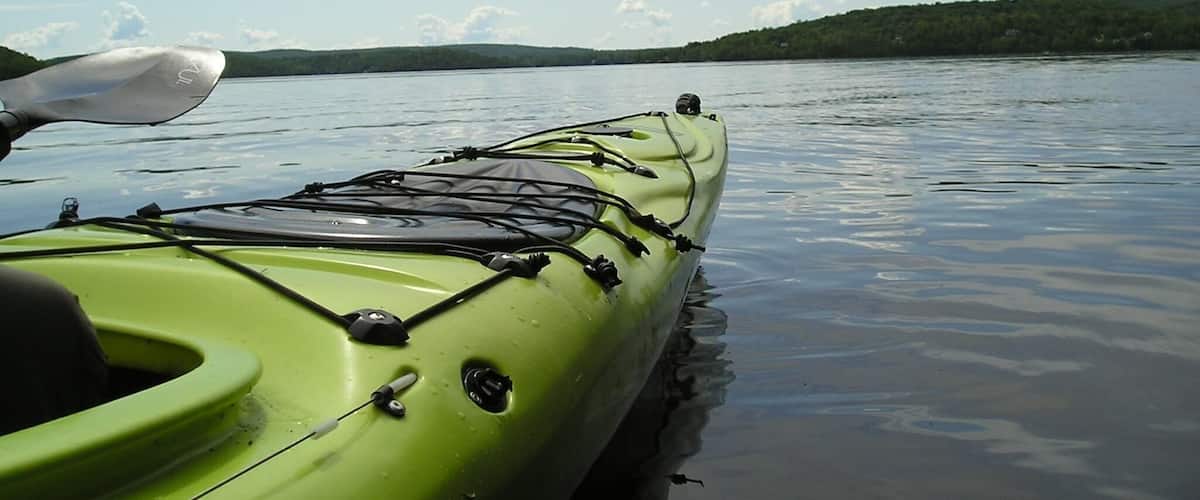 A green kayak on calm water with a forested shoreline in the background.