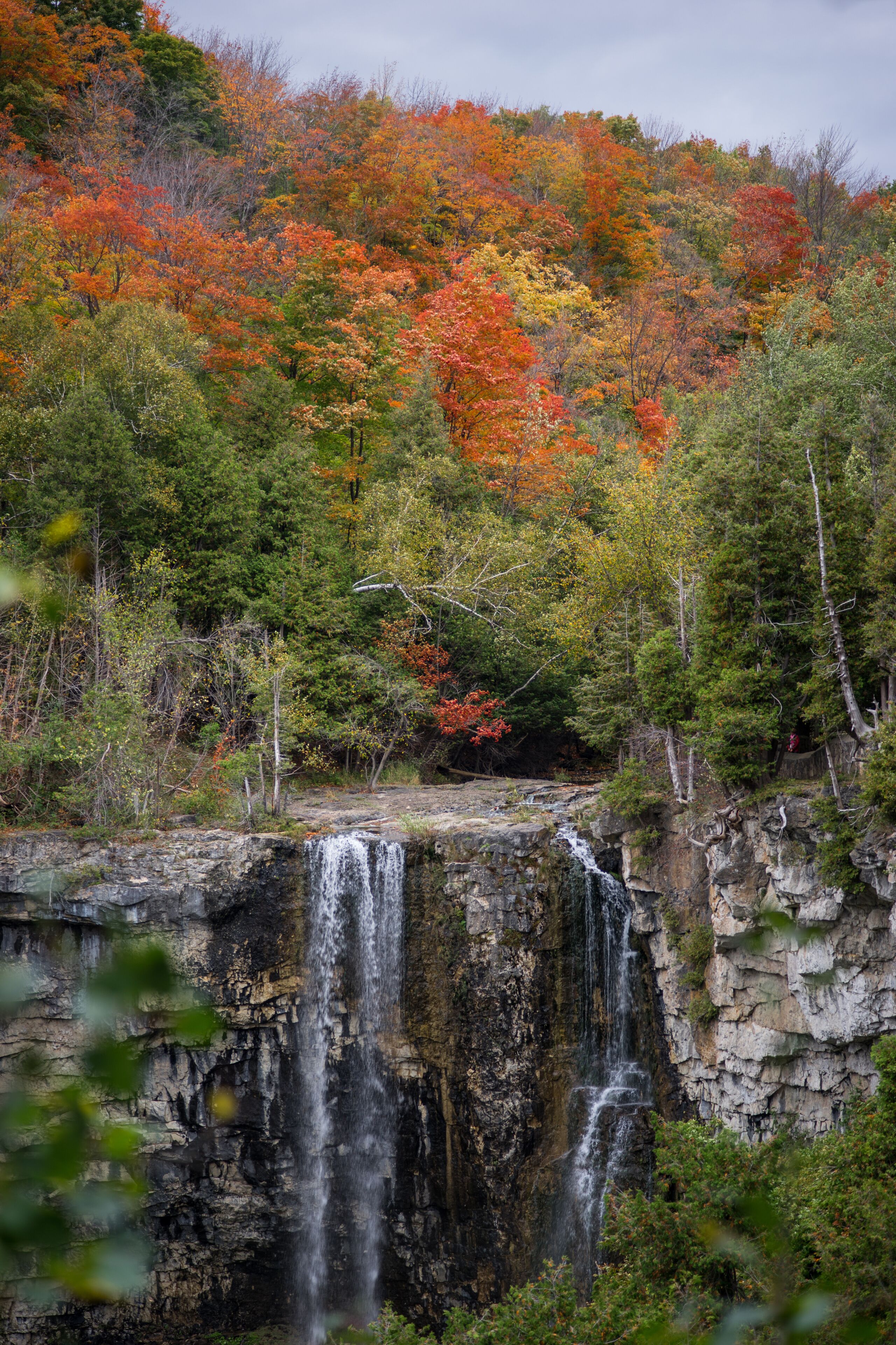 Une cascade d’eau se précipitant le long d’une falaise rocheuse, entourée d’un feuillage aux couleurs automnales.