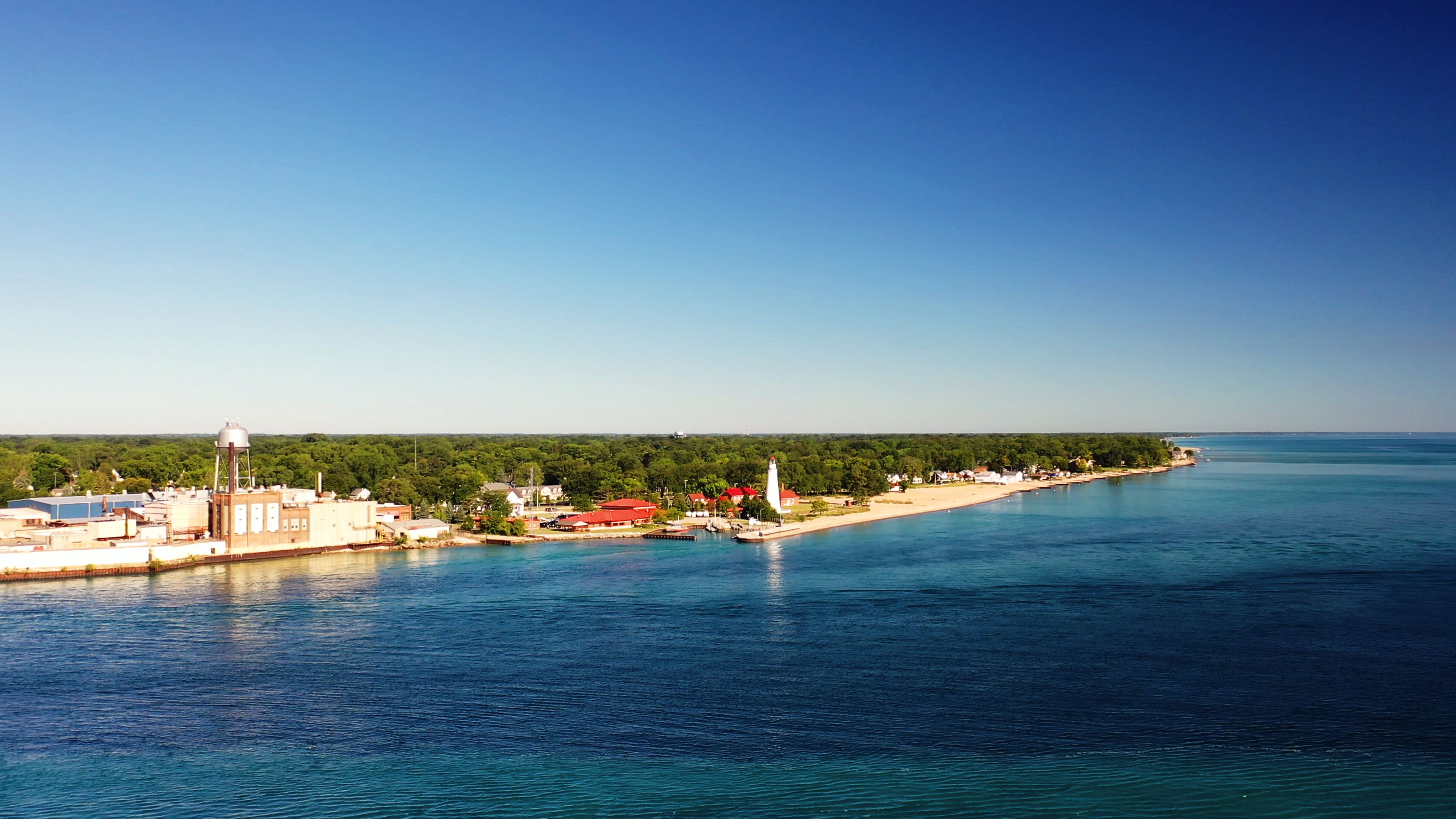 A coastal town with a lighthouse, water tower, and red-roofed buildings along the shoreline.