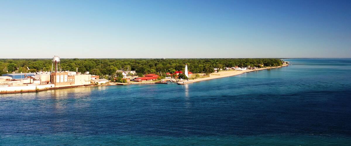 A coastal town with a lighthouse, water tower, and red-roofed buildings along the shoreline.