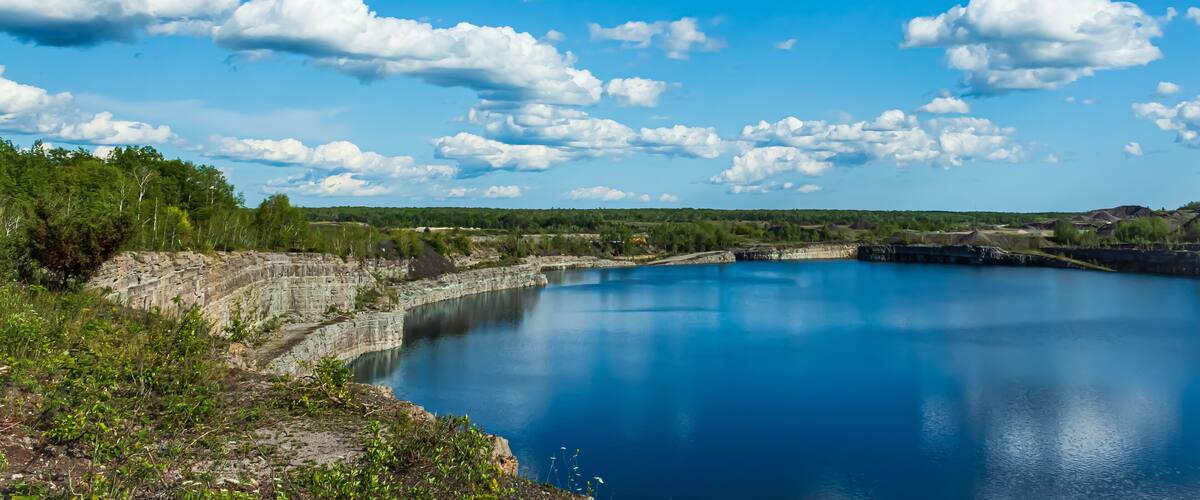 A serene lake surrounded by rocky cliffs and greenery under a clear blue sky with scattered clouds.