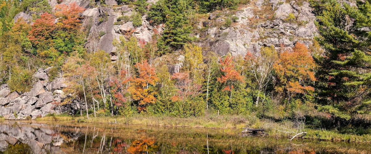A calm lake surrounded by autumn-colored trees and rocky terrain.