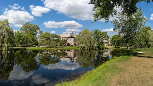 Un lac paisible dont les eaux reflètent les arbres et, au loin, un bâtiment historique.