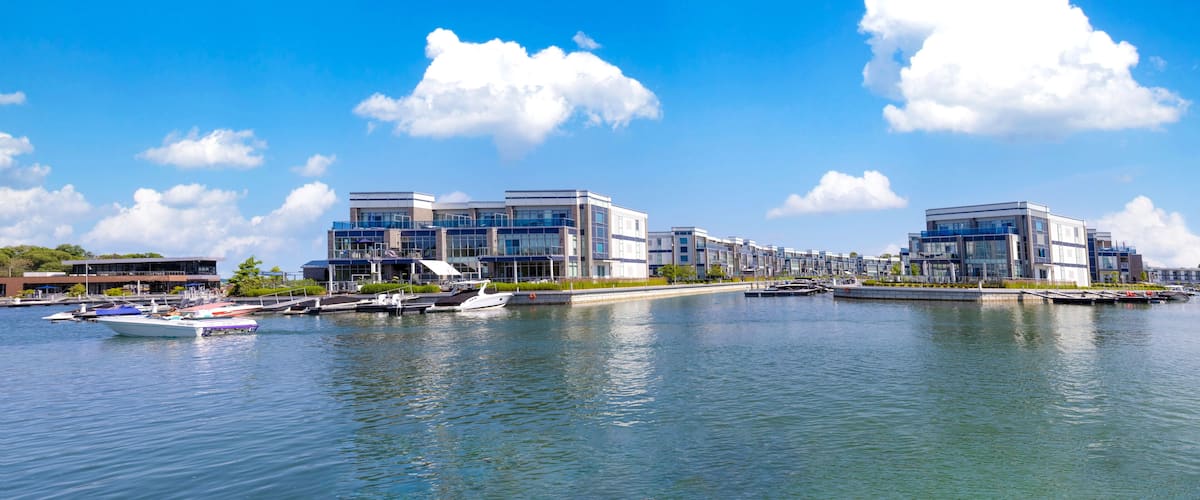 A marina with modern buildings, calm water, and a clear blue sky.