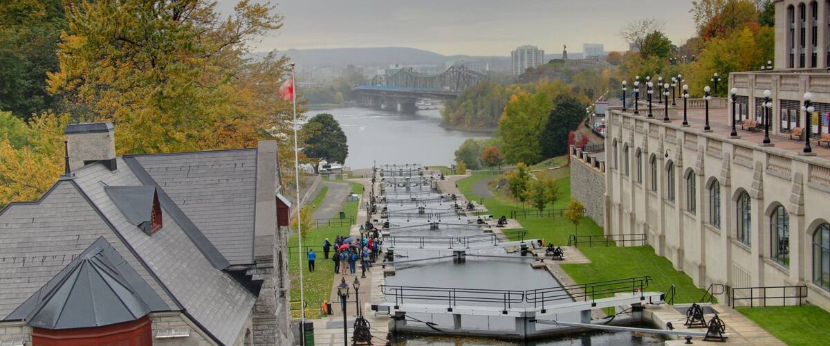A river with a lock system, a bridge in the background, and autumn foliage.