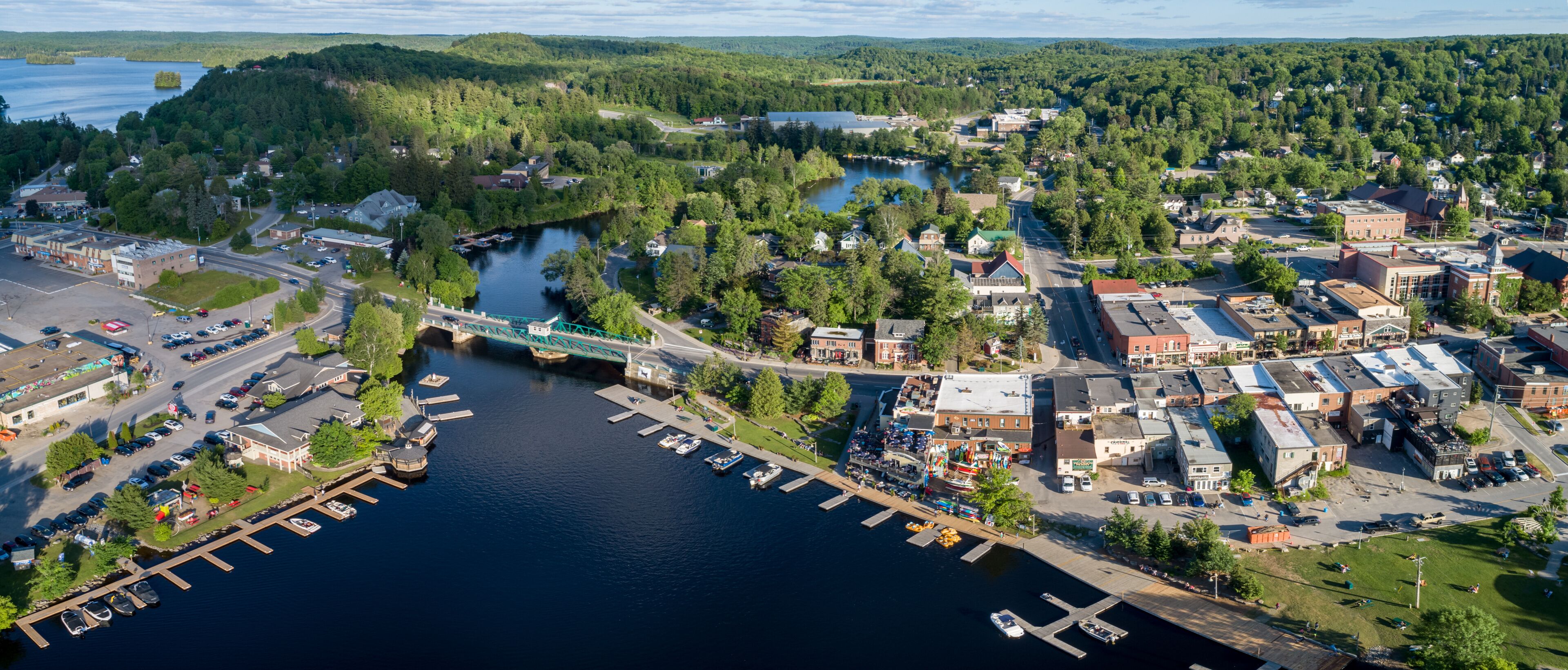 An aerial view of a riverside town with a bridge, docks, and surrounding greenery.