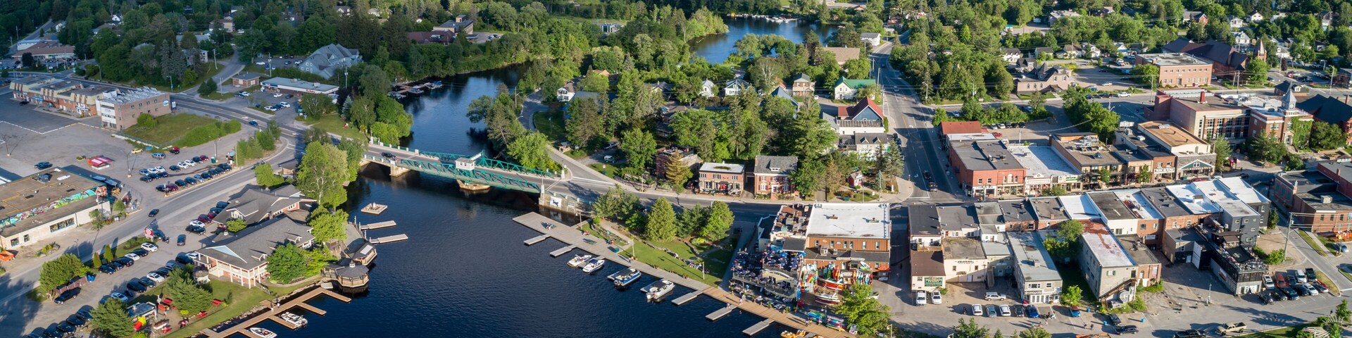 An aerial view of a riverside town with a bridge, docks, and surrounding greenery.