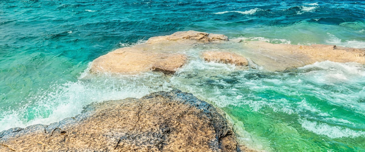 A rocky coastline with clear turquoise waters and a distant island.