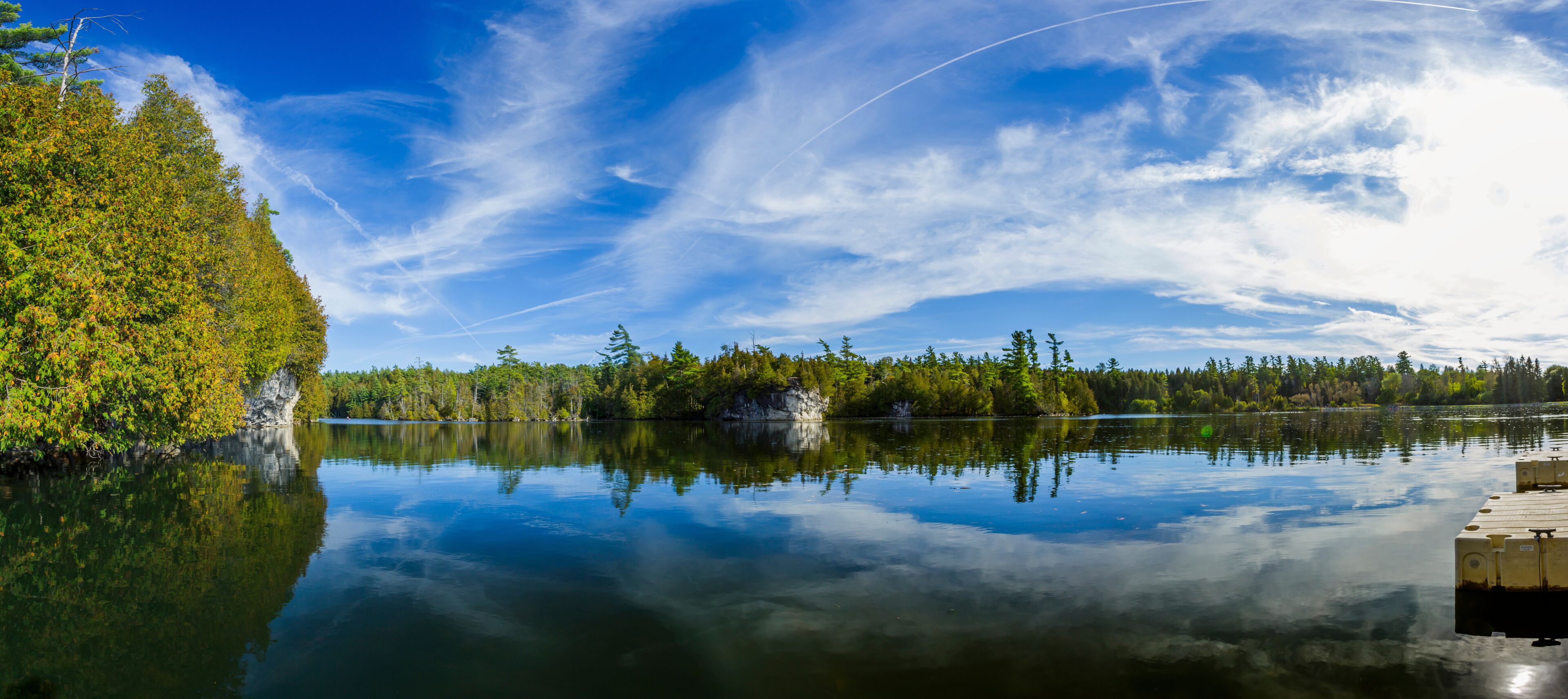 A calm lake with reflections of trees and a clear sky.