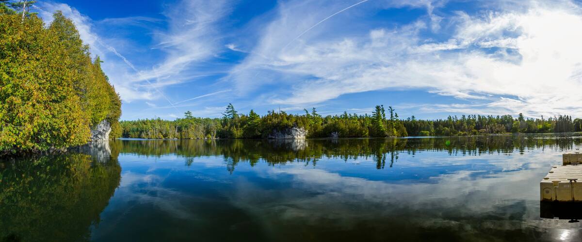A calm lake with reflections of trees and a clear sky.