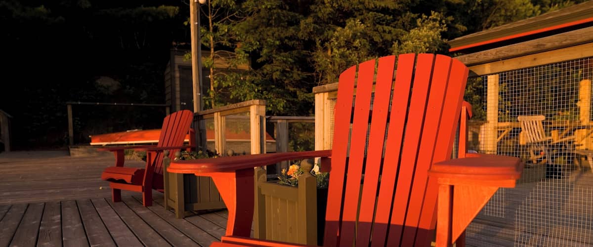 A wooden deck with red Adirondack chairs and a small table.