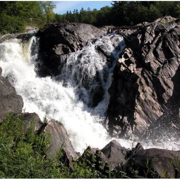 A waterfall cascading over rocky terrain surrounded by greenery.