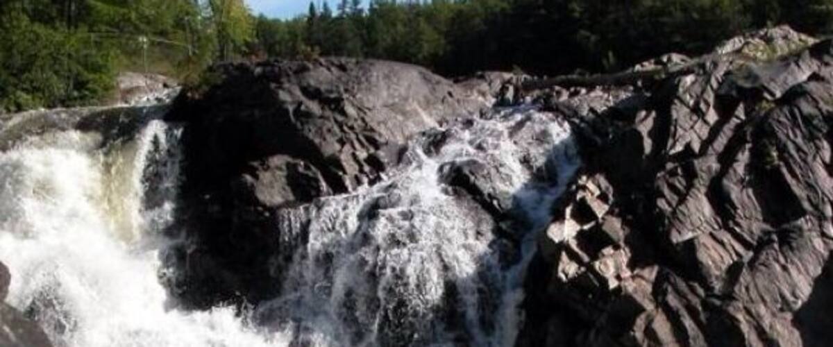 A waterfall cascading over rocky terrain surrounded by greenery.