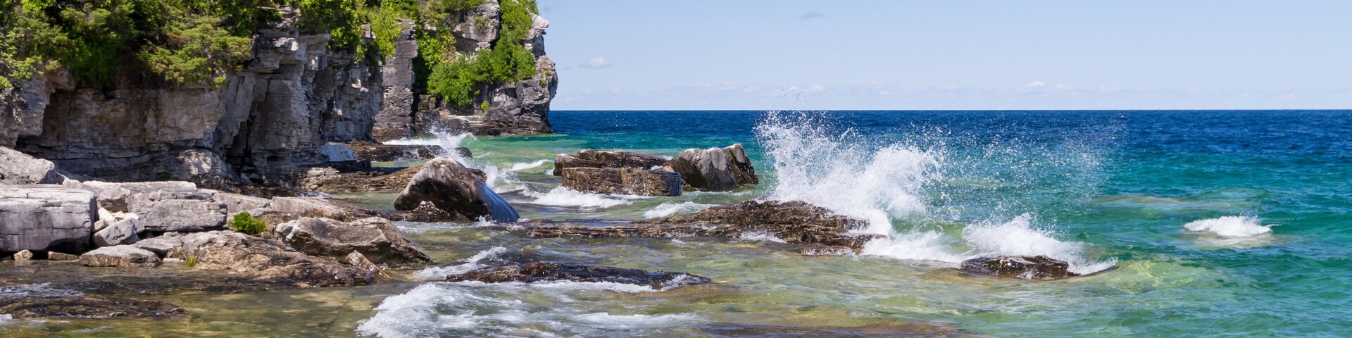 Una costa rocosa con agua cristalina, olas rompiendo contra las rocas y un acantilado cubierto de bosque.