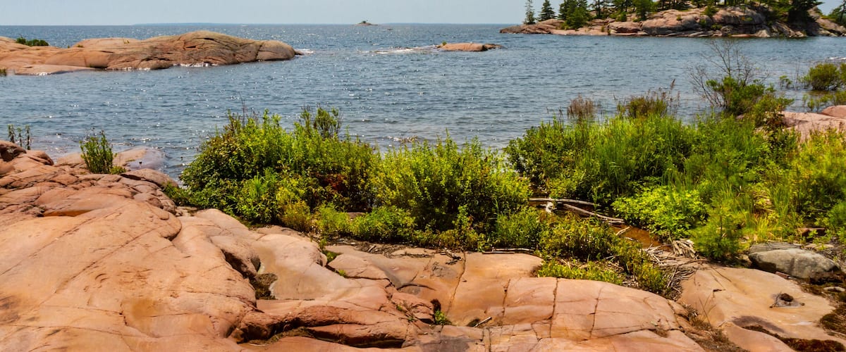 A rocky shoreline with clear water and a distant island with trees.