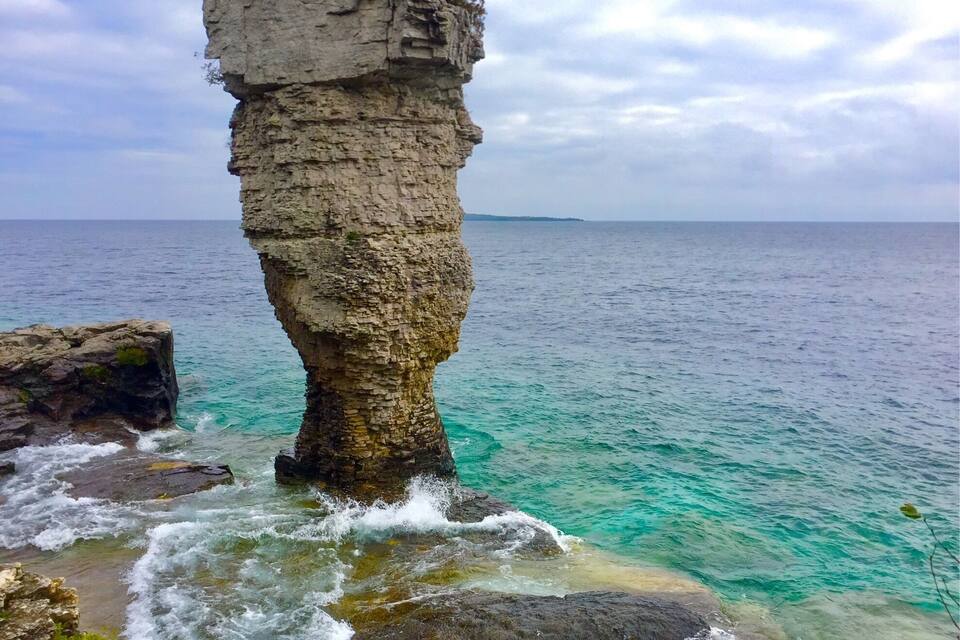Een rotsformatie aan de kust met helder turquoise water en een bewolkte lucht.