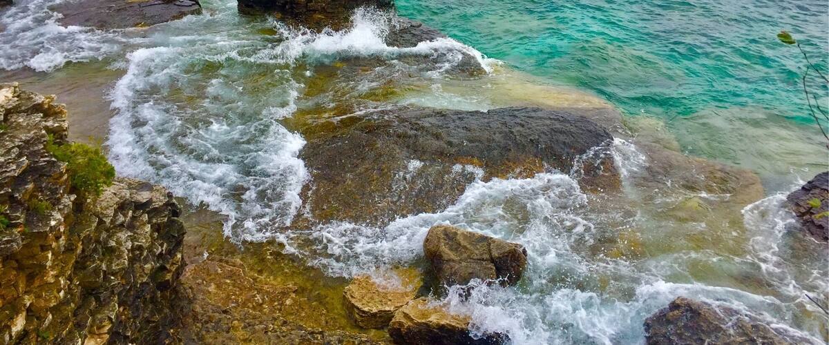 A coastal rock formation with clear turquoise waters and a cloudy sky.