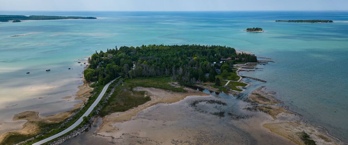 An aerial view of a forested island surrounded by clear blue waters.