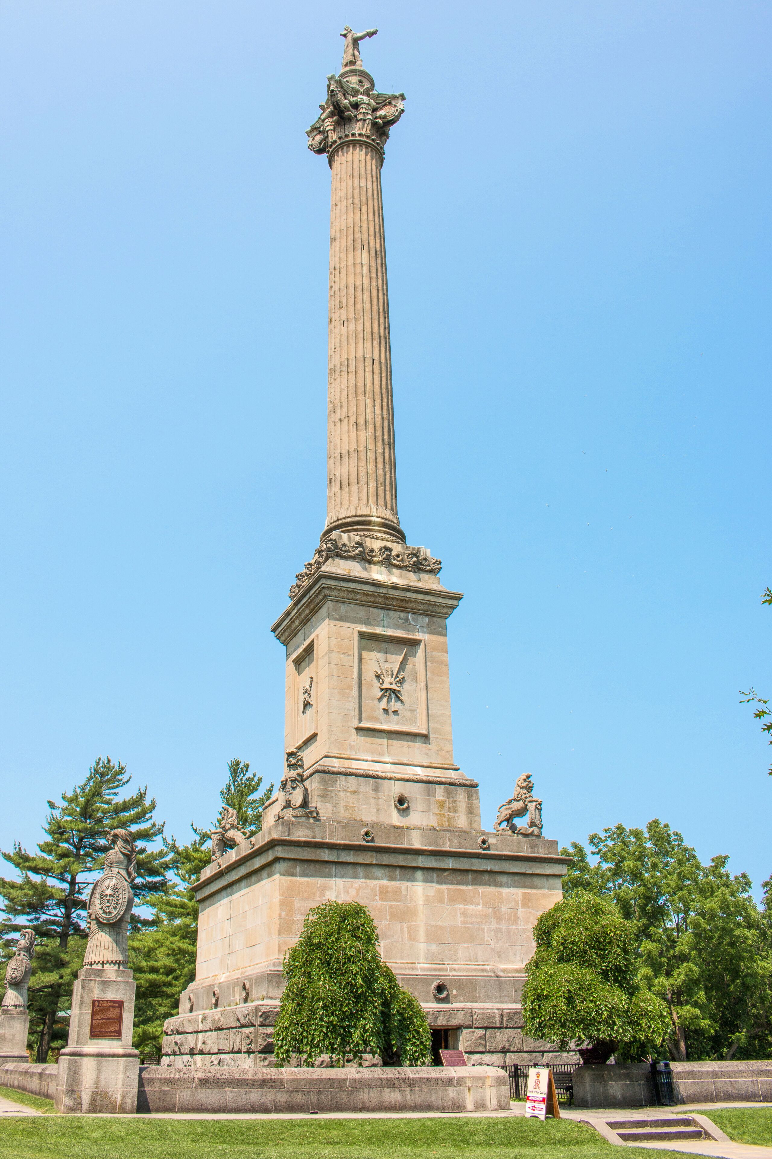 A tall, ornate monument with statues and a clock, surrounded by trees and a well-maintained lawn.
