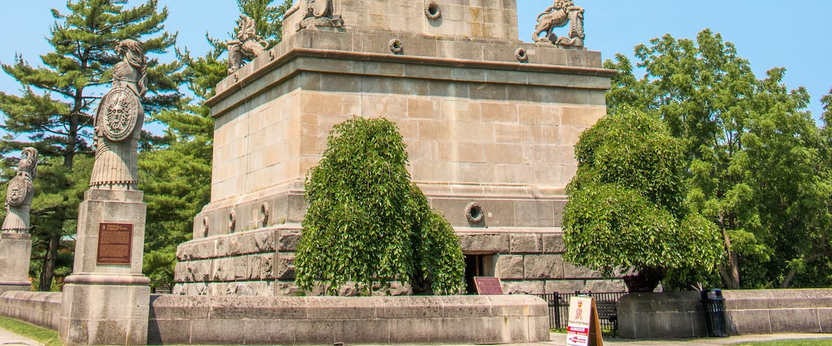 A tall, ornate monument with statues and a clock, surrounded by trees and a well-maintained lawn.