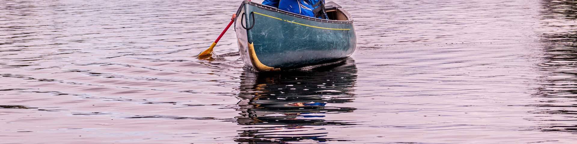 young woman paddling a green canoe solo on a river with trees clad in freshly fallen snow in the background room for text shot on the ottawa river in eastern ontario canada