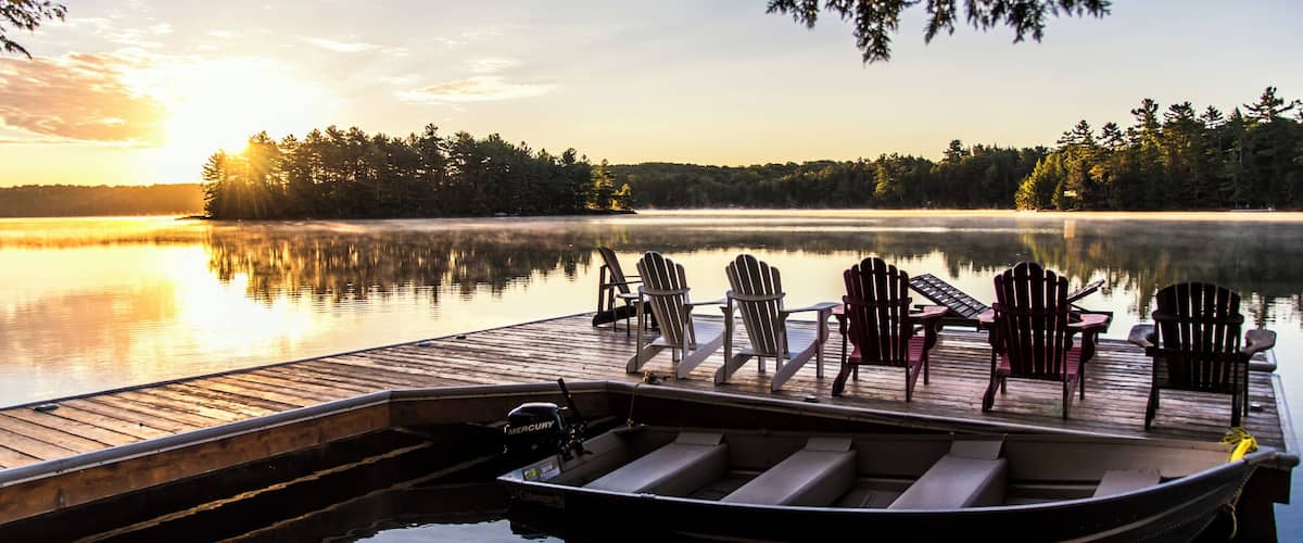 A wooden dock with chairs and a boat at a calm lake during sunset.