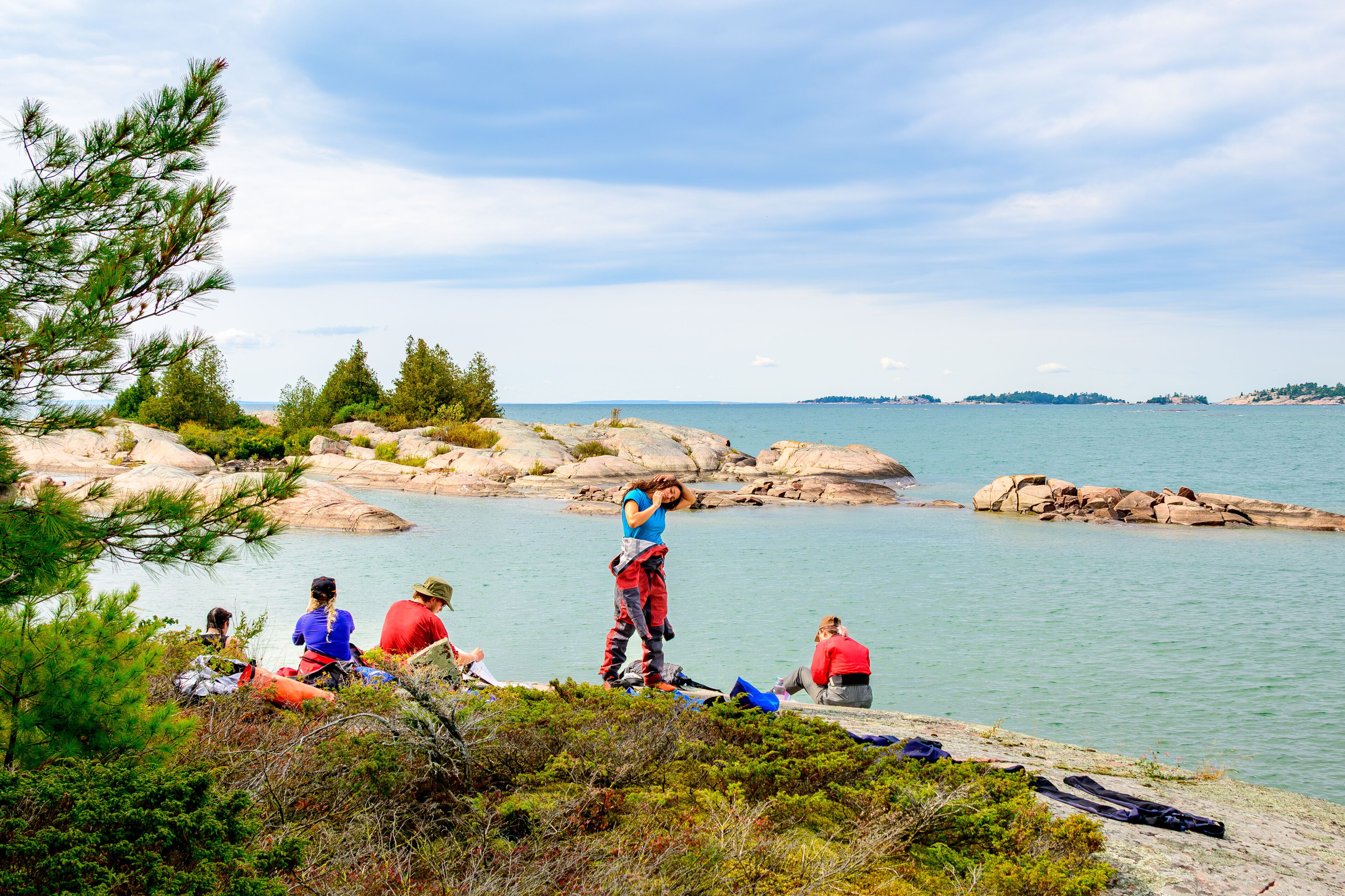 Stretching on the rocks: a young woman does yoga  in her drysuit shot during a sea kayak expedition on Georgian Bay in fall rocks trees and clouds in background room for text