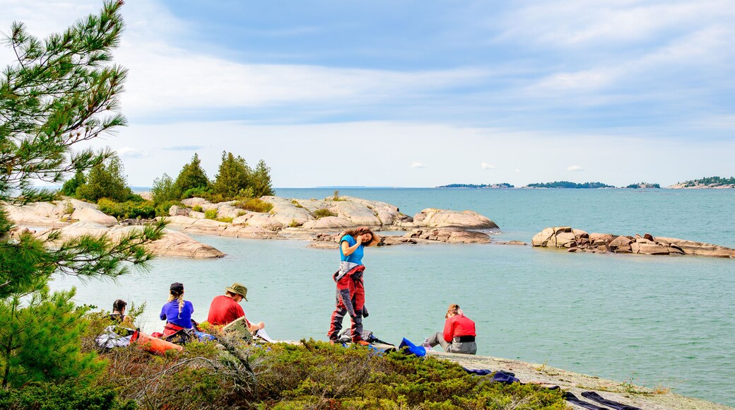 Stretching on the rocks: a young woman does yoga in her drysuit shot during a sea kayak expedition on Georgian Bay in fall rocks trees and clouds in background room for text
