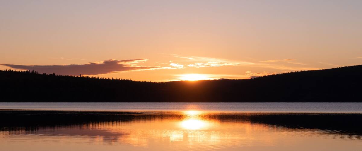 A sunset over a calm lake with a forested hill in the background.