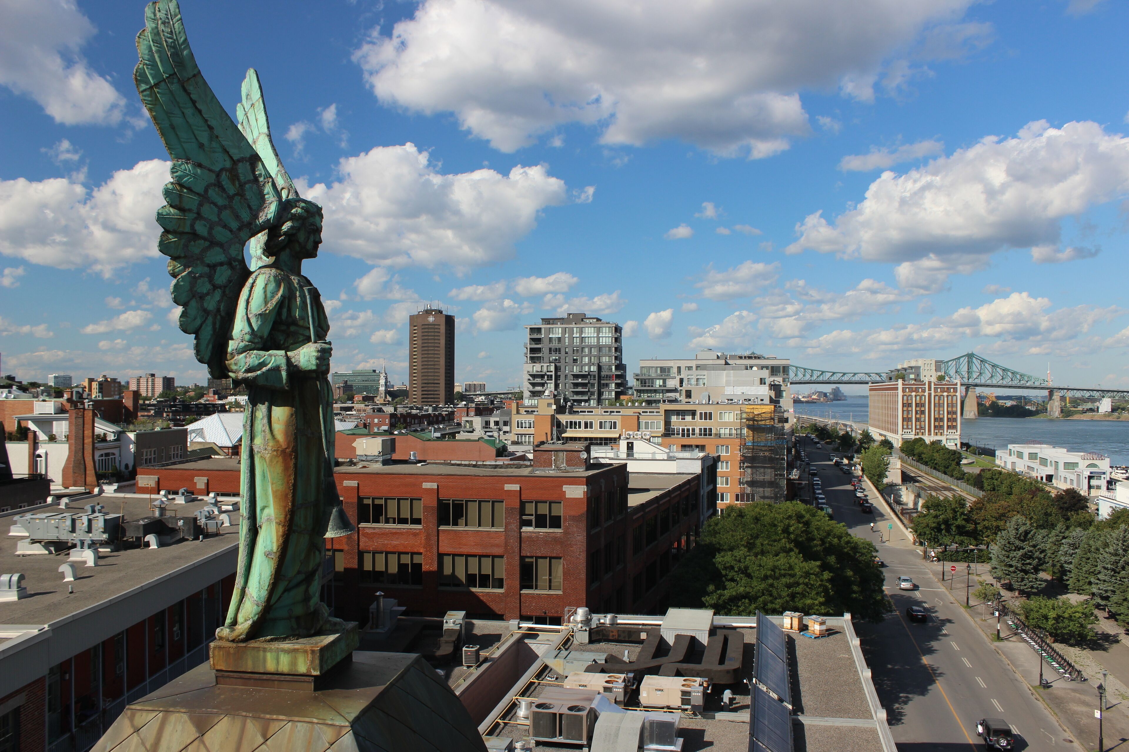 A statue of an angel with wings overlooking a cityscape with buildings, a river, and a bridge.