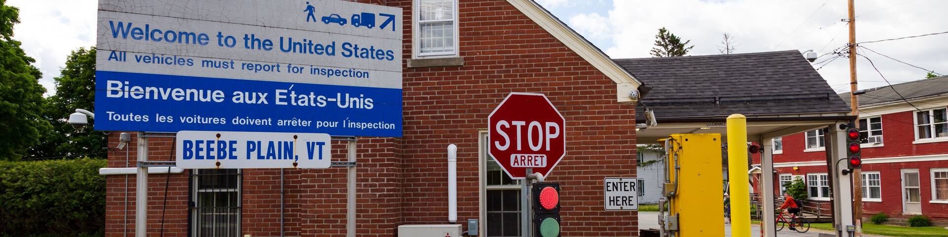 A building with a stop sign, a traffic light, and a sign welcoming visitors to the United States.