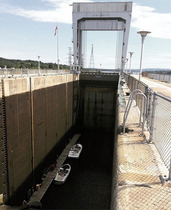 A lock with two boats inside, a metal walkway, and a fence.