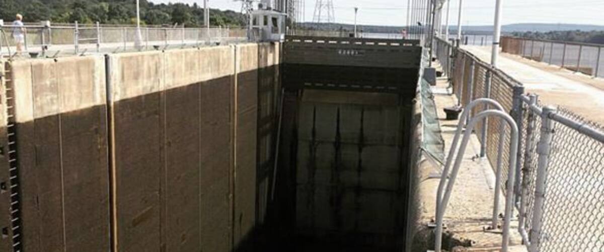 A lock with two boats inside, a metal walkway, and a fence.