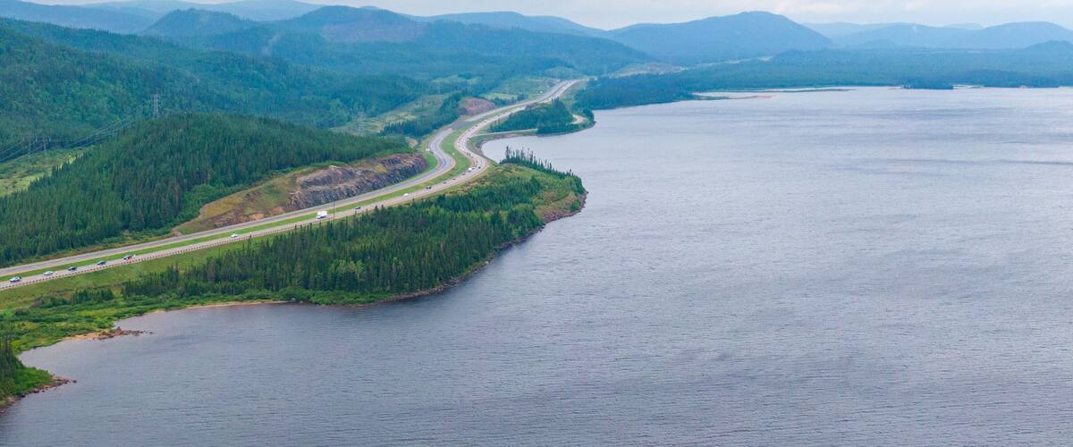 A winding road along a river surrounded by dense forests and mountains.