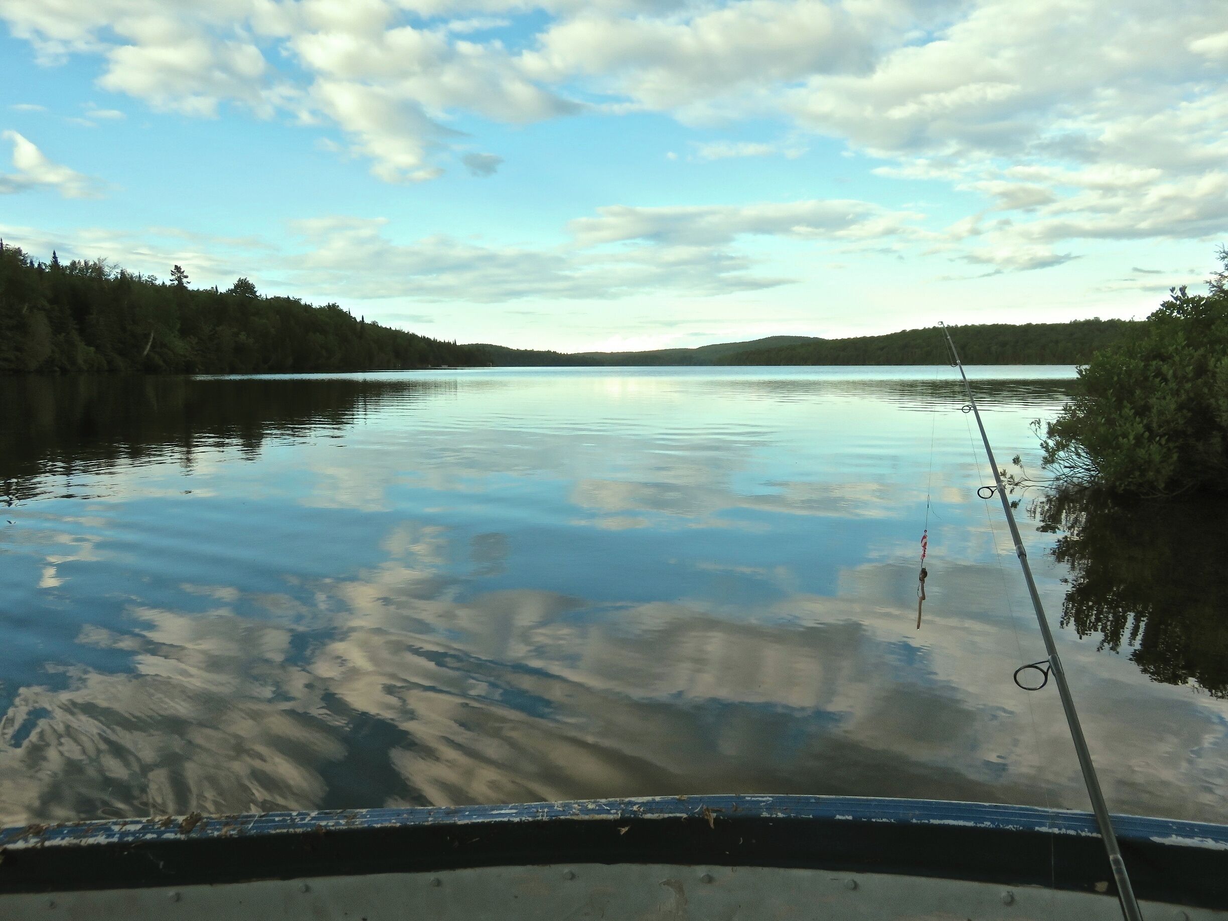 A calm lake with a fishing rod, surrounded by forested hills.