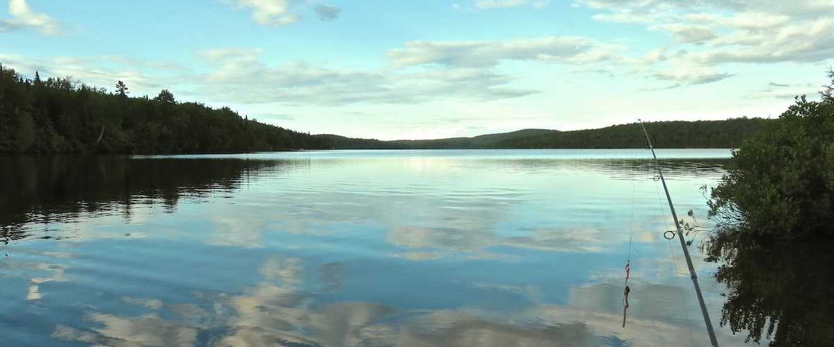 A calm lake with a fishing rod, surrounded by forested hills.