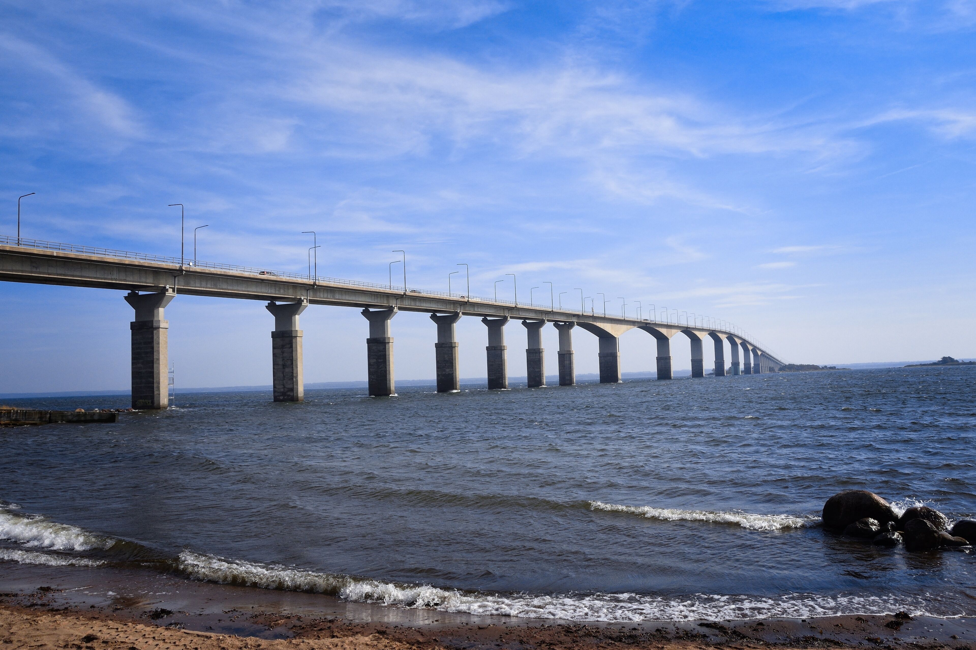 A long bridge over a body of water with waves crashing onto the shore.