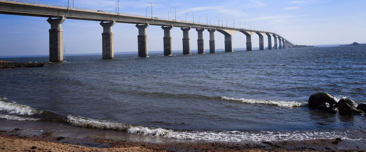 A long bridge over a body of water with waves crashing onto the shore.